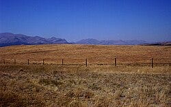 A field with a fence and mountains in the background

AI-generated content may be incorrect.
