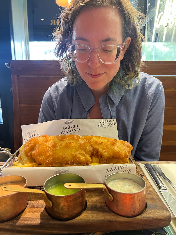 photos of Katie on vacation in London with Chris, seeing Les Mis, kissing in Bath, drinking tea, eating gluten free fish and chips, seeing a statue from DDLJ, and freezing at a football match.