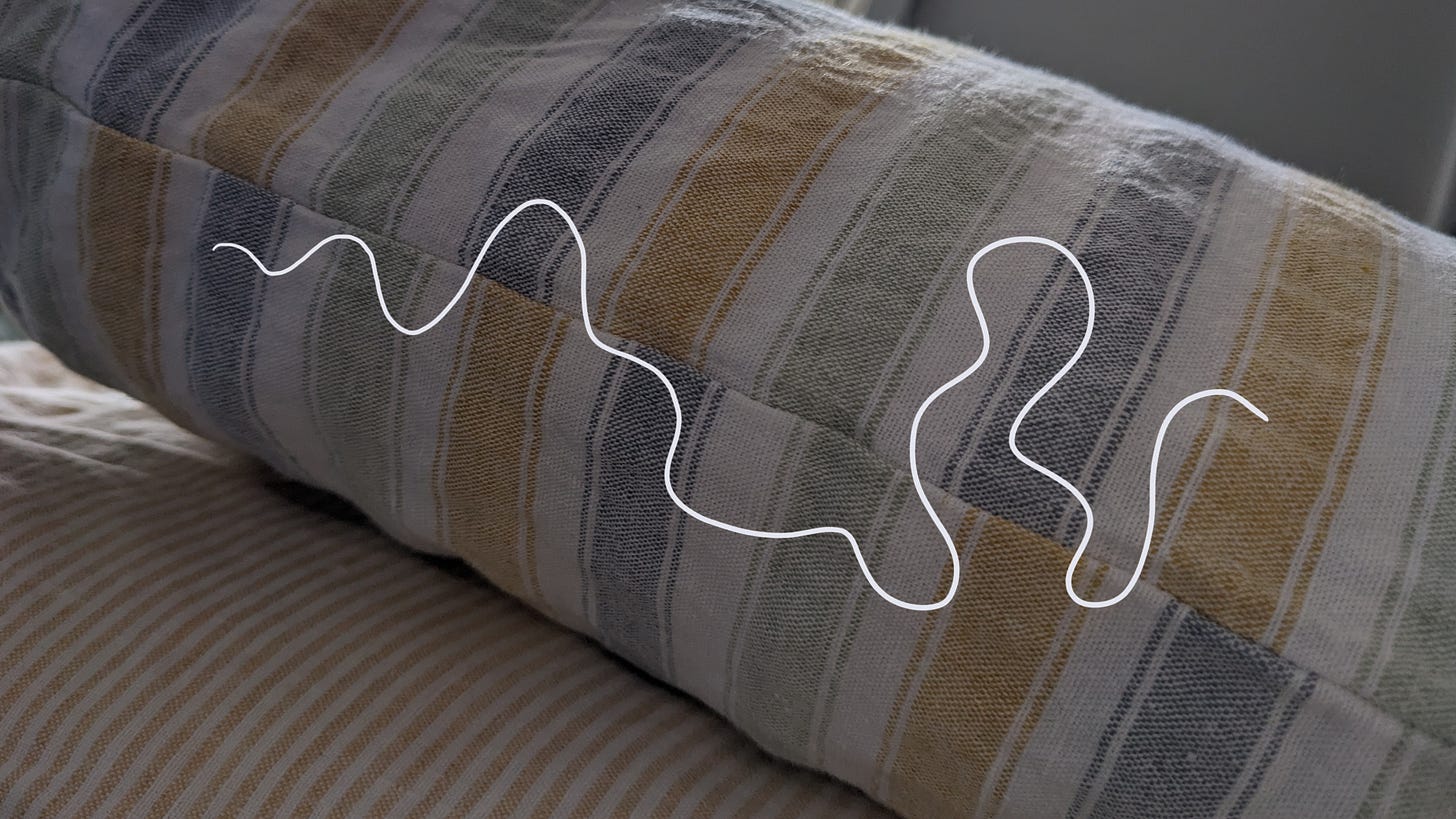 Image shows the view of the side of a pillow, from the perspective of someone lying in bed. A bed-rest eye view. Over the top is a white wobbly line, depicting a non-linear journey.