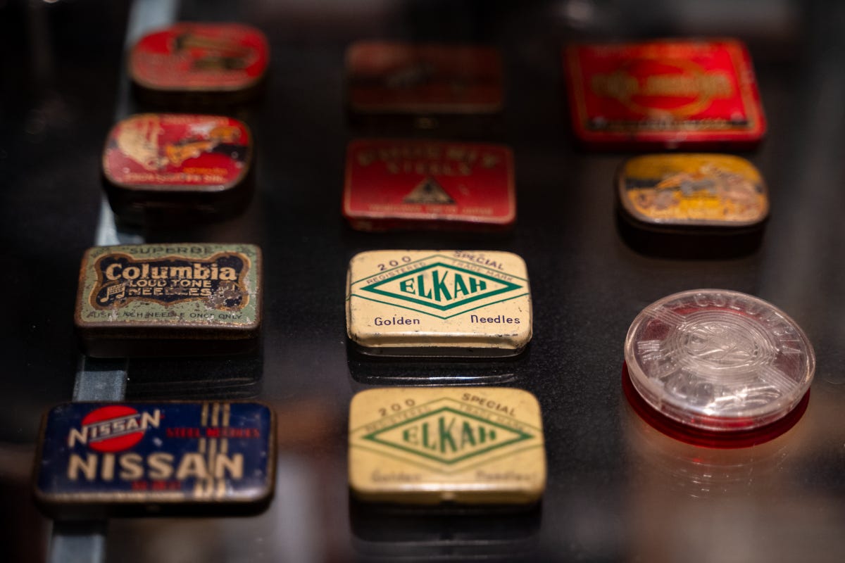 Antique, multicolored tin record needle cases arrayed on a glass shelf