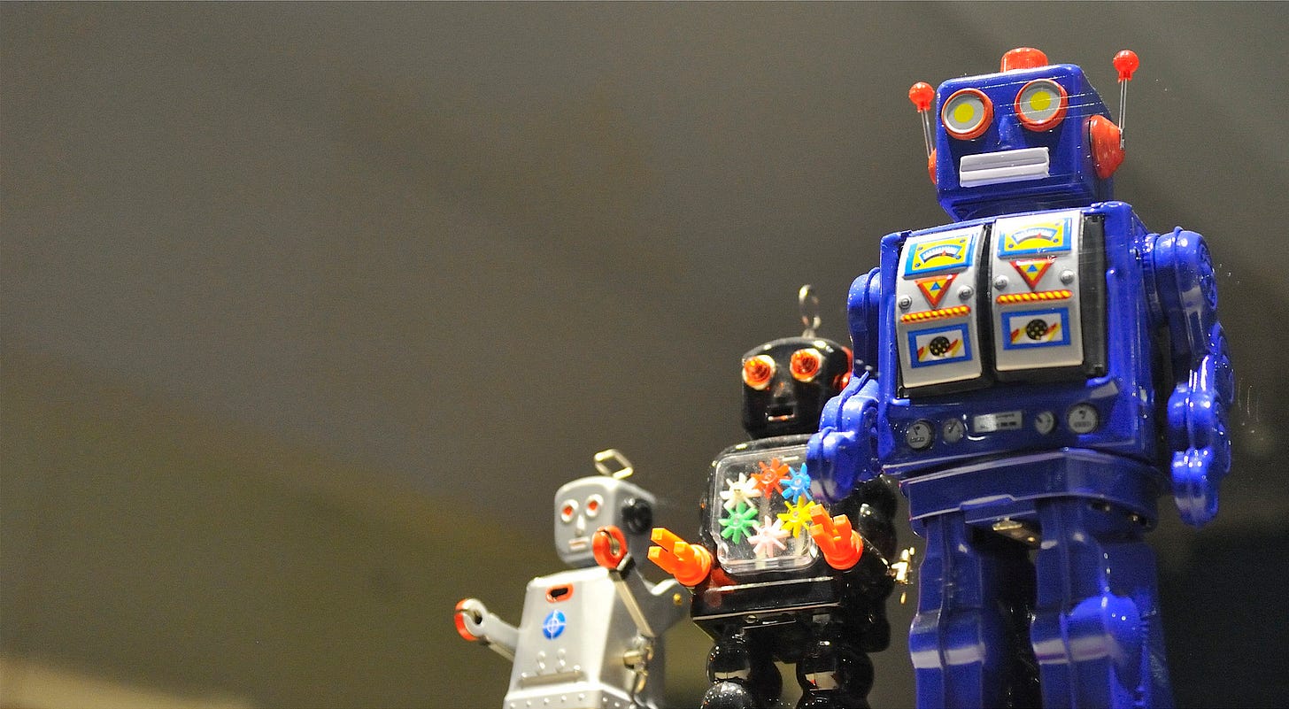 Three brightly colored toy robots in cartoonish humanoid form stand in a line against a dark background. Three brightly colored toy robots in cartoonish humanoid form stand in a line against a dark background.