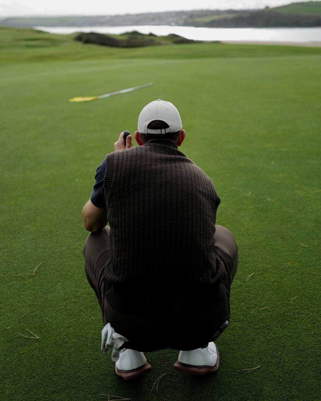 A person kneeling on a golf course

Description automatically generated