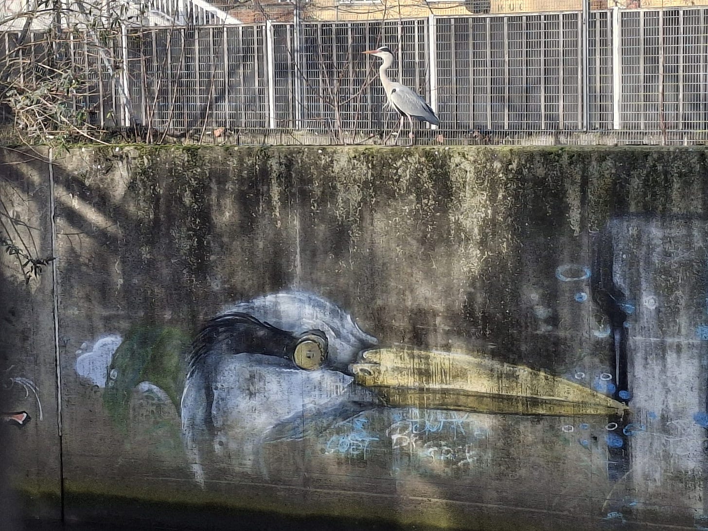 A heron sits on the wall above the mural of the Dave Heron A heron sits on the wall above the mural of the Dave Heron