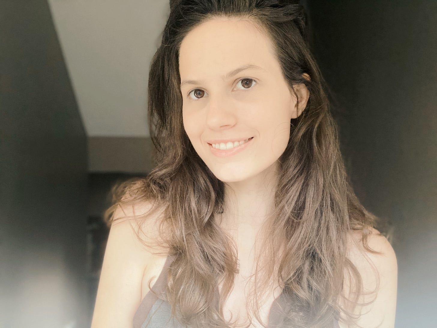Olivia Muenz, a white woman with long brown hair and brown eyes, is smiling and wearing an olive-colored, sleeveless top. She is in sunlight in front of a darker background. Olivia Muenz, a white woman with long brown hair and brown eyes, is smiling and wearing an olive-colored, sleeveless top. She is in sunlight in front of a darker background.