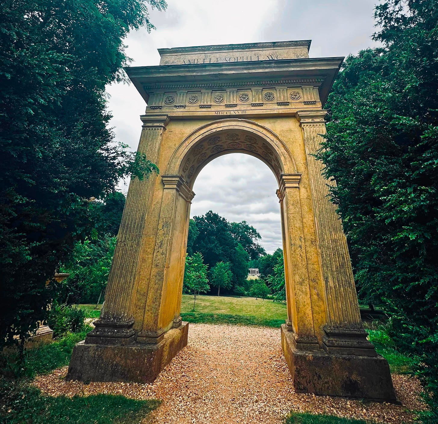 Stone archway framed by trees, opening onto a quiet path