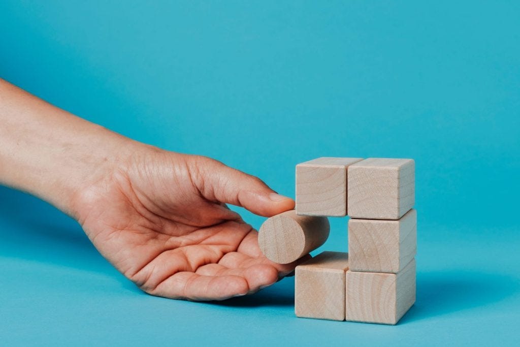 A stock image of a hand trying to fit a cylindrical block into a tower of square blocks