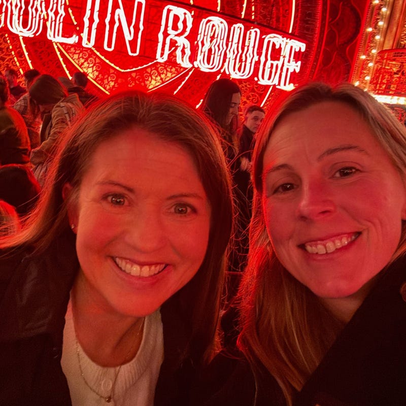 Amy Juli and her sister-in-law smiling for a selfie with the Moulin Rouge! stage in the background
