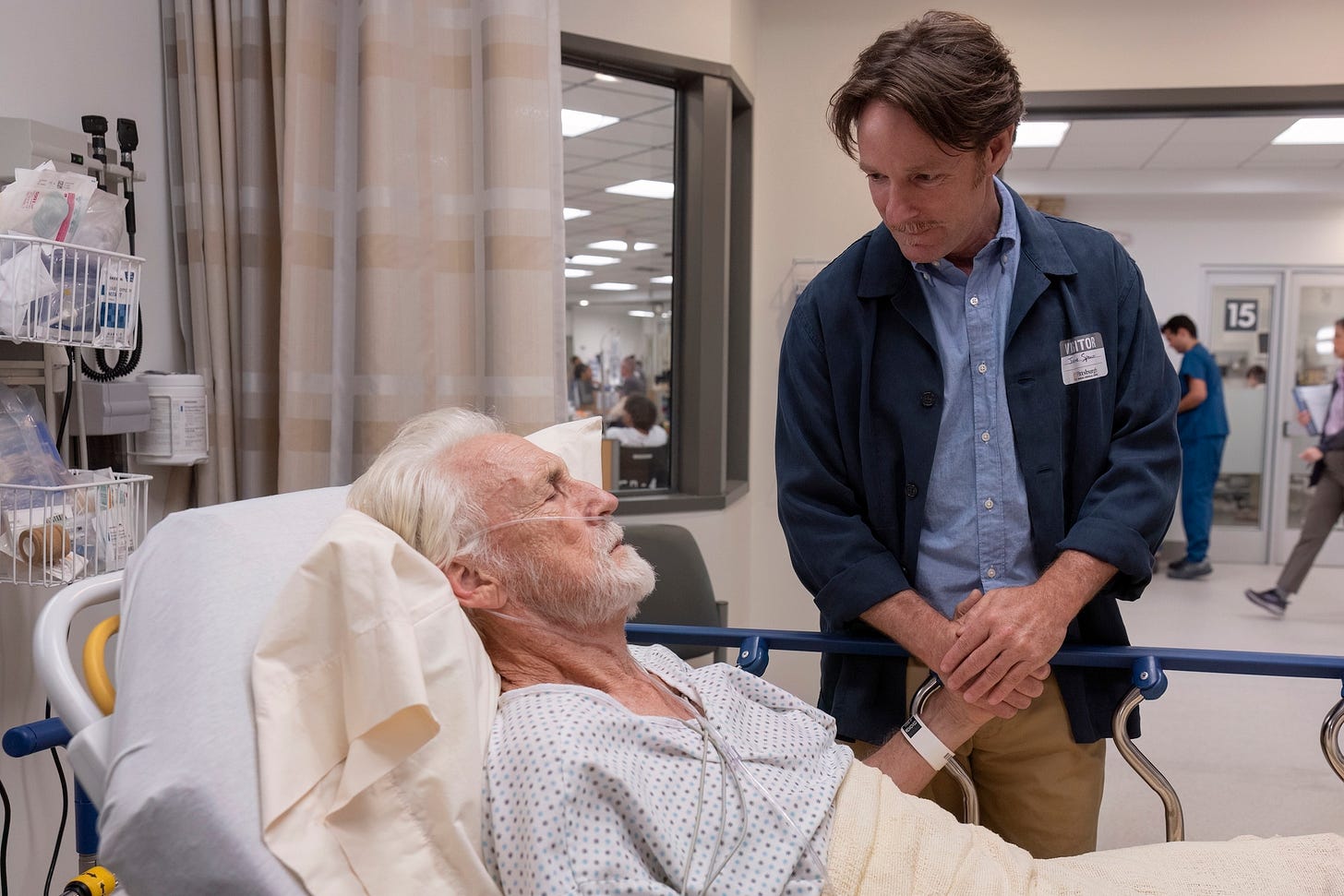A man stands next to an older man in a hospital bed A man stands next to an older man in a hospital bed