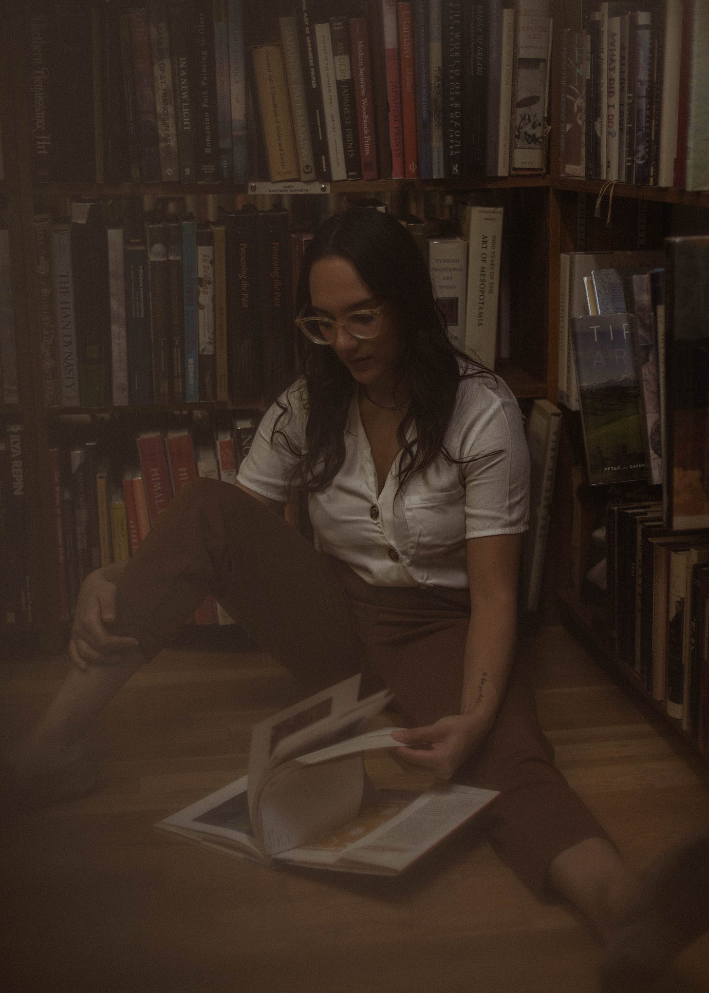 mia in front of book shelves on the floor reading a book