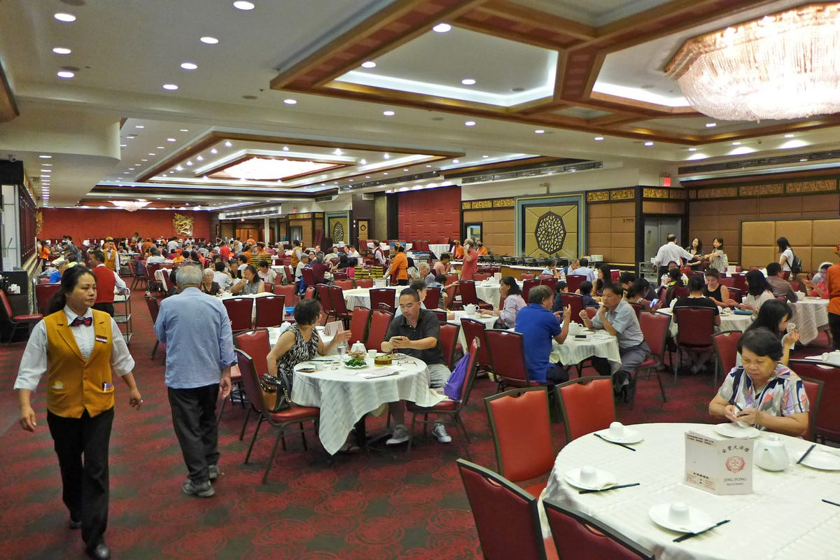 Jing Fong’s dining room with large, communal round tables and a red-and-green floor is filled with diners. Jing Fong’s dining room with large, communal round tables and a red-and-green floor is filled with diners.