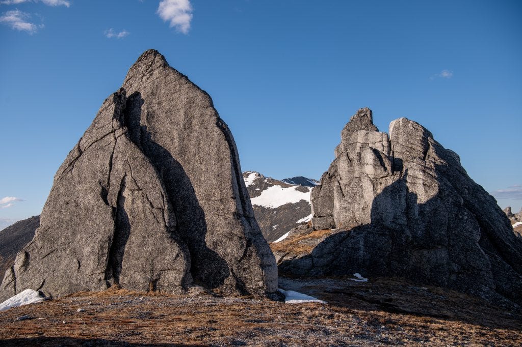 Two large granite spires rise from a ridge against a deep blue sky, a snow-streaked peak visible in the gap between them.