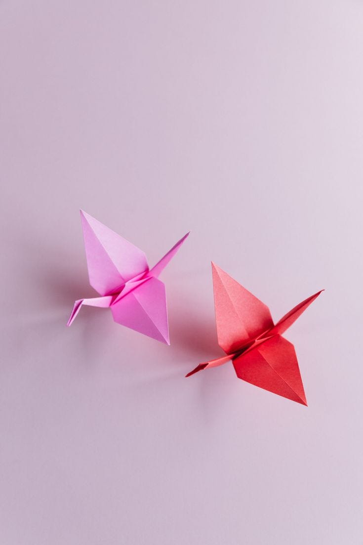 This may contain: two pink origami birds sitting side by side
