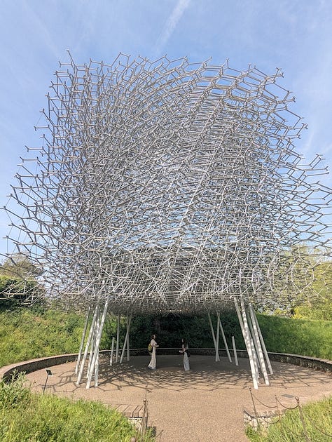 Three views of The Hive at Kew Gardens, a large aluminium lattice structure rising from a grassy landscape, shown from a distance, from beneath, and looking up through its circular interior.