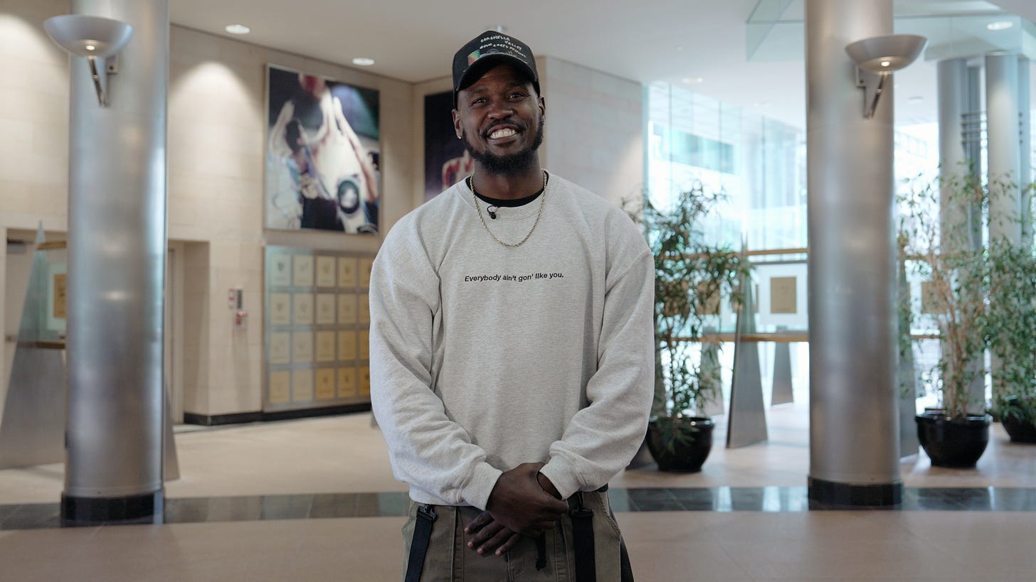 Matt Maxey, a Black man, wearing a black hat and a grey sweater with the words "Everybody aint gon' like you. He smiles. Matt Maxey, a Black man, wearing a black hat and a grey sweater with the words "Everybody aint gon' like you. He smiles.