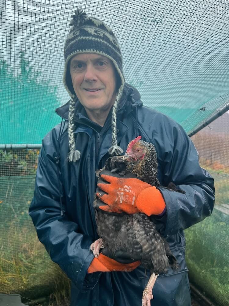 Ian, dressed in waterproof jackte and Norwegian hat, holds a chicken