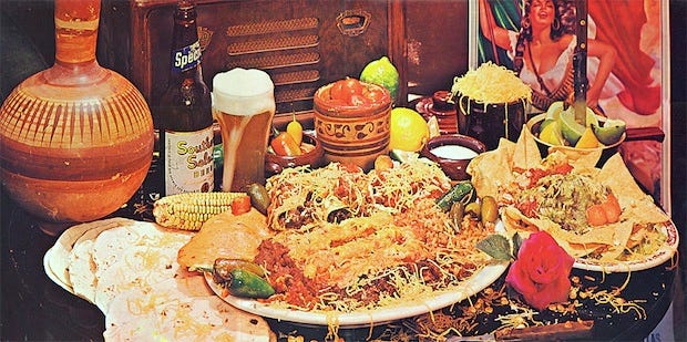 Photo of a gigantic Tex-Mex feast. There are flour tortillas, enchiladas, rice and beans, and tacos. There is a glass of beer and a clay jug. There is a picture of a woman dressed a Mexican revolutionary. Photo of a gigantic Tex-Mex feast. There are flour tortillas, enchiladas, rice and beans, and tacos. There is a glass of beer and a clay jug. There is a picture of a woman dressed a Mexican revolutionary.