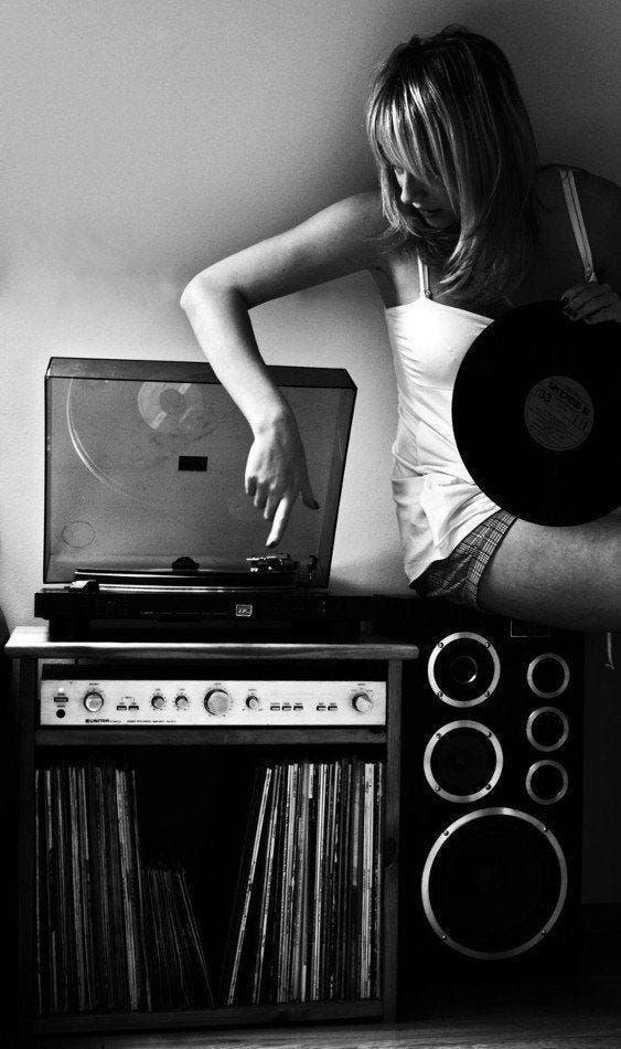 This may contain: a woman in white shirt standing next to record player and turntable with vinyl on it