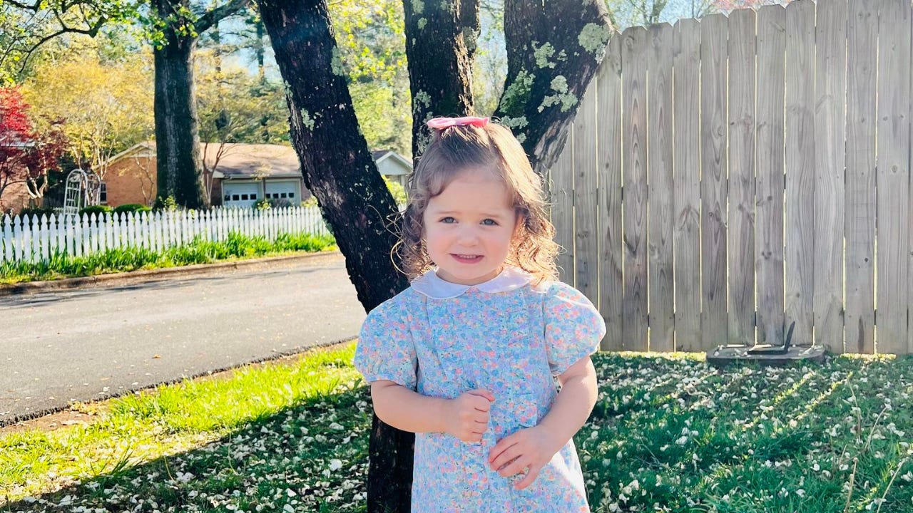 A little girl standing outside on a sunny day.