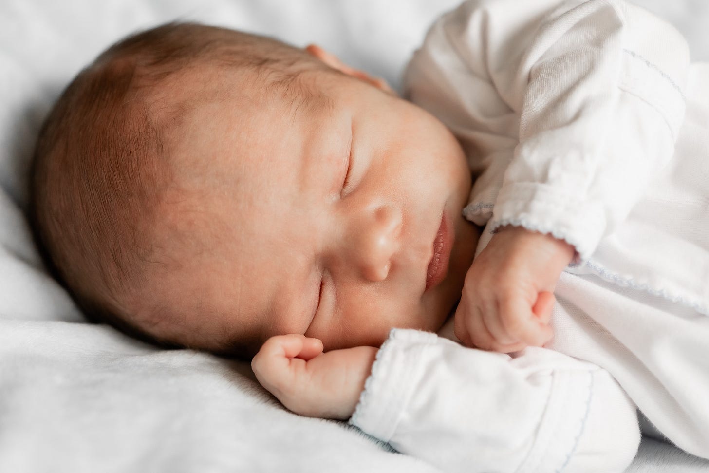 a newborn baby boy sleeping in a white onesie