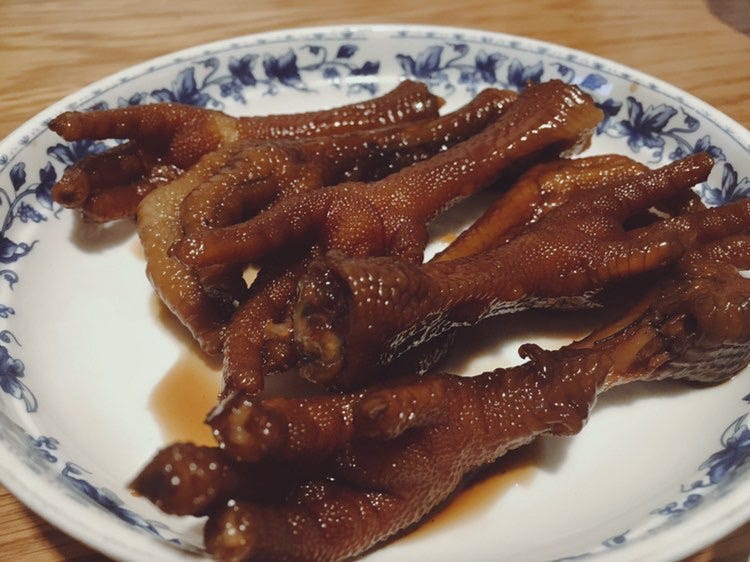 A pile of six braised chicken feet in a small white dish patterned with blue flowers around its rim