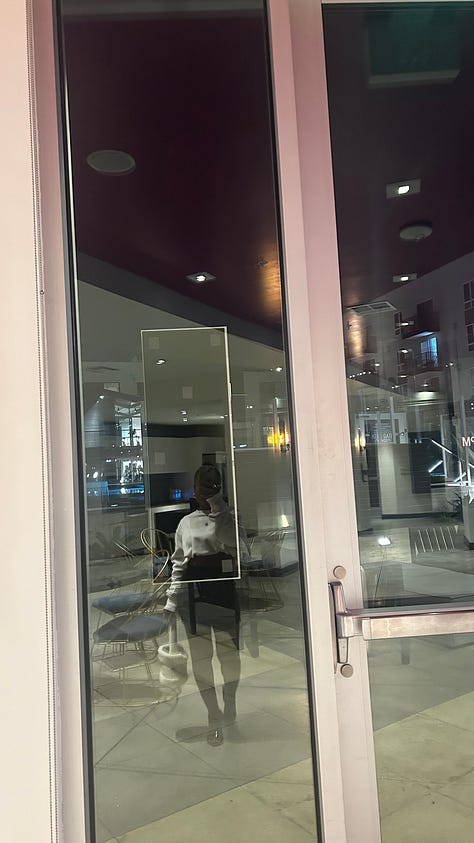 A cinematic series anchored in deep reds and soft shadow: two sculptural red lounge chairs beneath a large abstract canvas; a single orange rose placed against textured wood flooring; a blurred bouquet of roses glowing under streaks of warm light; a nighttime self-portrait reflected in glass doors; and a tightly framed cluster of red roses resting on a neutral surface. The compositions emphasize symmetry, negative space, reflection, and saturated color, creating a quiet narrative of intimacy, interior space, and becoming.