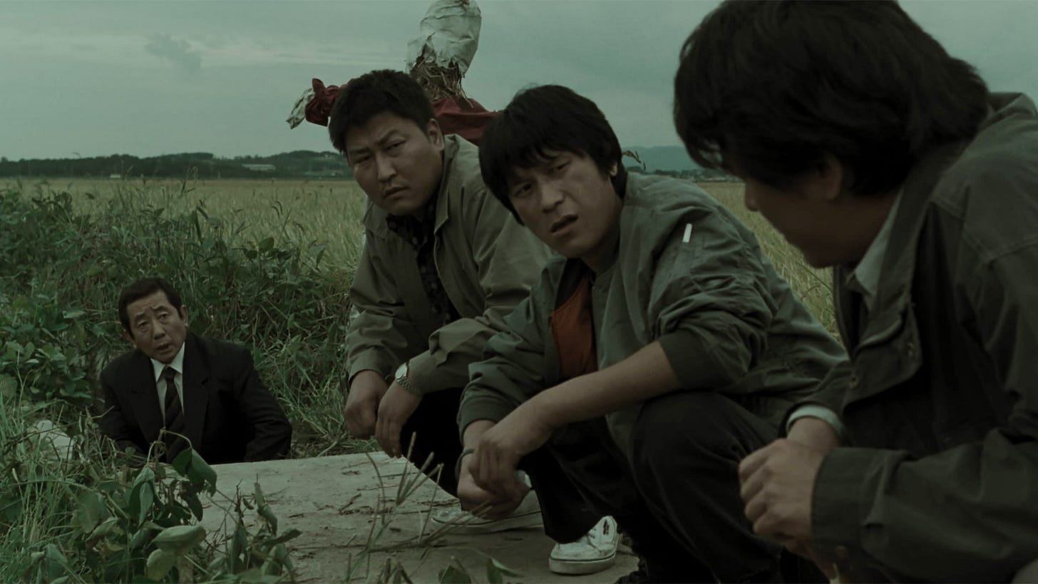A shot from Bong Joon Ho's Memories of Murder, depicting several detectives crouching near a storm drain where a corpse has been found.