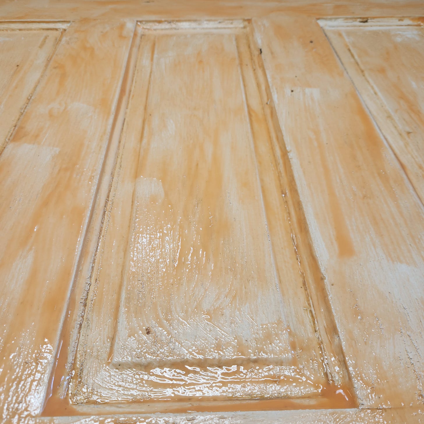 Close up picture of an old door with a thick layer of orange chemical stripper.