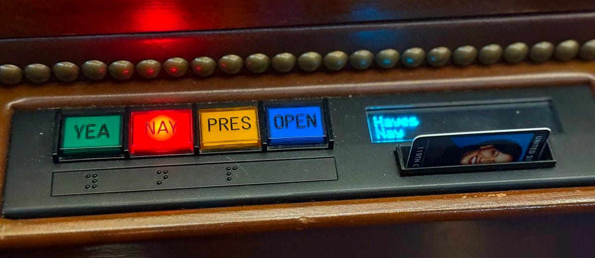 The image shows a close-up of a voting console used in the U.S. House of Representatives. The console has four buttons labeled "YEA", "NAY", "PRES", and "OPEN", each with corresponding colors (green, red, yellow, and blue). The "NAY" button is illuminated, indicating a "No" vote. To the right of the buttons, there is a small digital display showing "House Time" and a slot with a card inserted, likely for identification. The post text by Jahana Hayes (@RepJahanaHayes) states "Hayes votes No ❌", providing context that Representative Jahana Hayes has voted against a measure. The image shows a close-up of a voting console used in the U.S. House of Representatives. The console has four buttons labeled "YEA", "NAY", "PRES", and "OPEN", each with corresponding colors (green, red, yellow, and blue). The "NAY" button is illuminated, indicating a "No" vote. To the right of the buttons, there is a small digital display showing "House Time" and a slot with a card inserted, likely for identification. The post text by Jahana Hayes (@RepJahanaHayes) states "Hayes votes No ❌", providing context that Representative Jahana Hayes has voted against a measure.