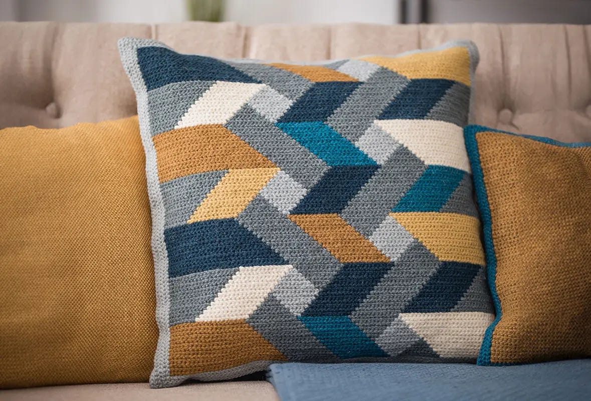 The Geometric Cushion is on a beige sofa in the middle of two other yellow cushions