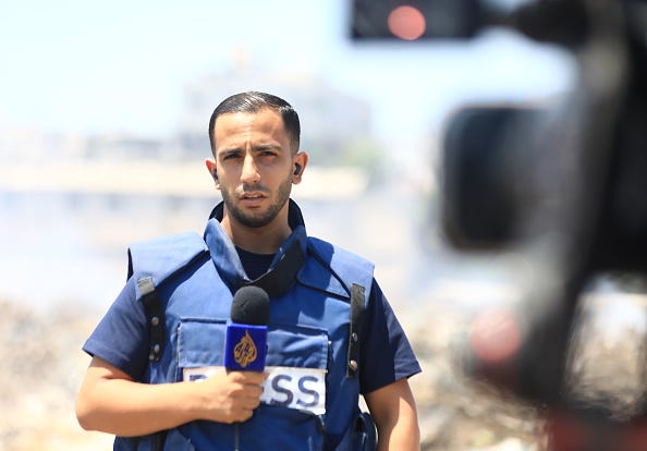Image of Anas Al-Sharif in a press vest holding an Al-Jazeera microphone