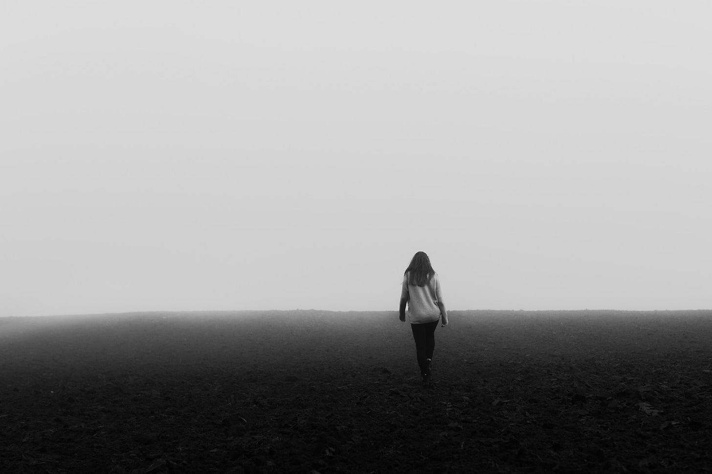 Woman walking alone along barren, gray landscape. Photo credit: Lucija Ros