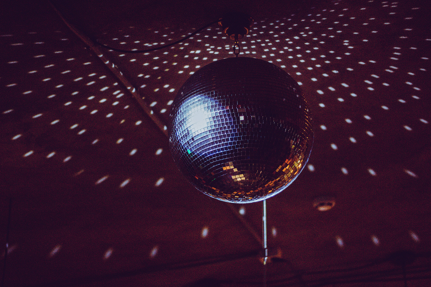 Close-up of a silver disco ball scattering light across a dark and shadowy ceiling. Close-up of a silver disco ball scattering light across a dark and shadowy ceiling.