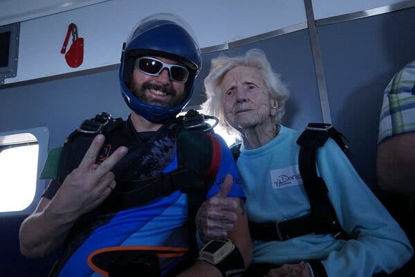 Derek Baxter wears a helmet and sunglasses and smiles next to Dorothy Hoffner, who is wearing a baby blue sweater.