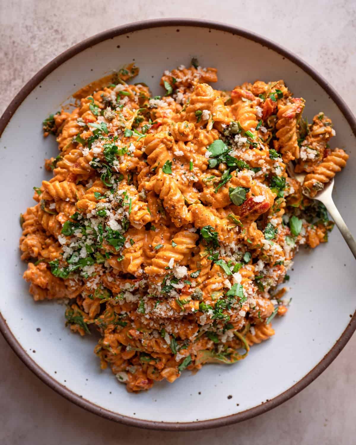 vegan roasted red pepper pasta salad in a speckled white bowl, fork tucked into pasta. vegan roasted red pepper pasta salad in a speckled white bowl, fork tucked into pasta.