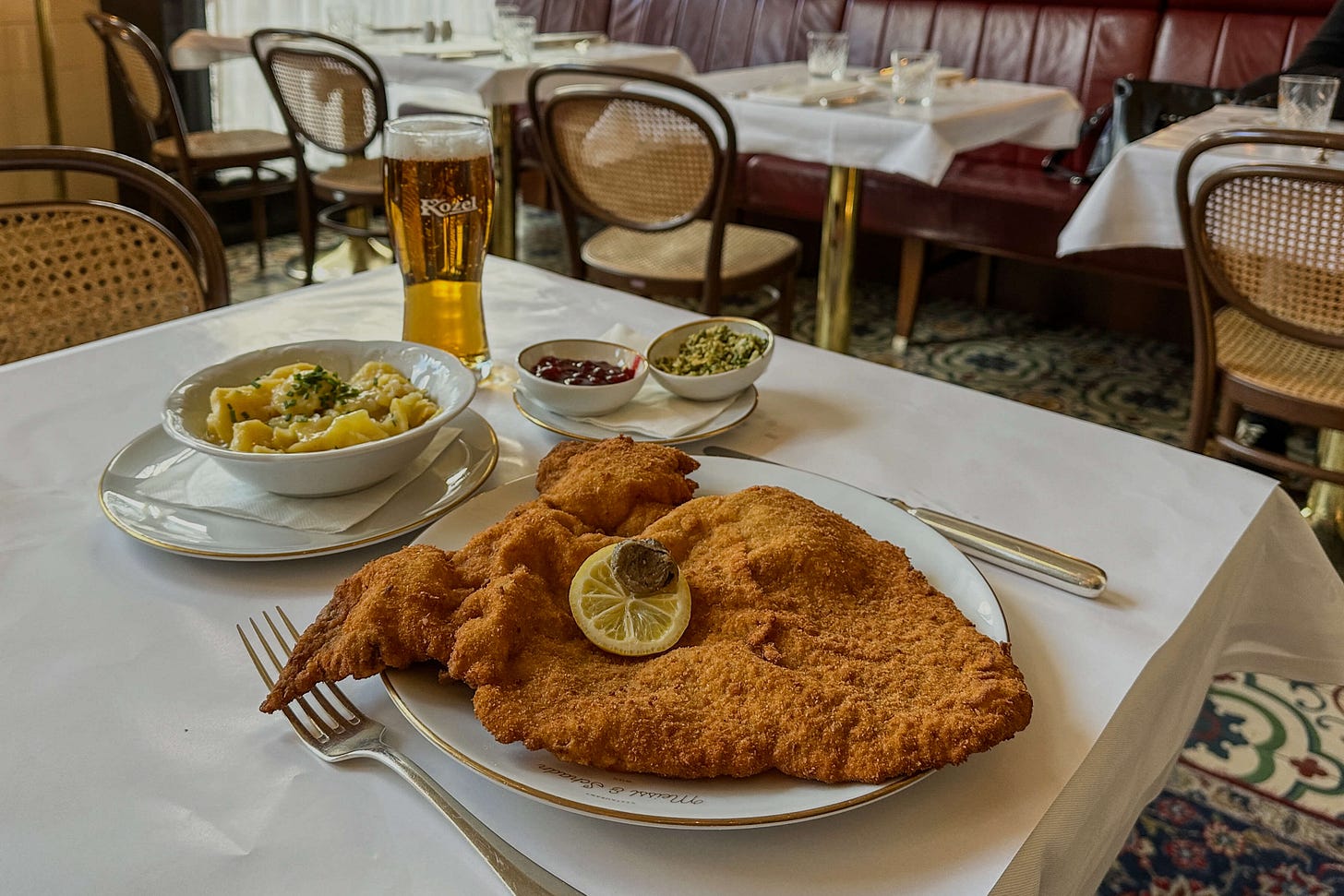 Gedeckter Tisch in einem Wiener Restaurant mit einem grossen Wiener Schnitzel auf weissem Teller, garniert mit Zitronenscheibe. Dazu werden Erdäpfelsalat, Preiselbeeren und Kapern serviert, die klassischen Wiener Garnitur. Gedeckter Tisch in einem Wiener Restaurant mit einem grossen Wiener Schnitzel auf weissem Teller, garniert mit Zitronenscheibe. Dazu werden Erdäpfelsalat, Preiselbeeren und Kapern serviert, die klassischen Wiener Garnitur.