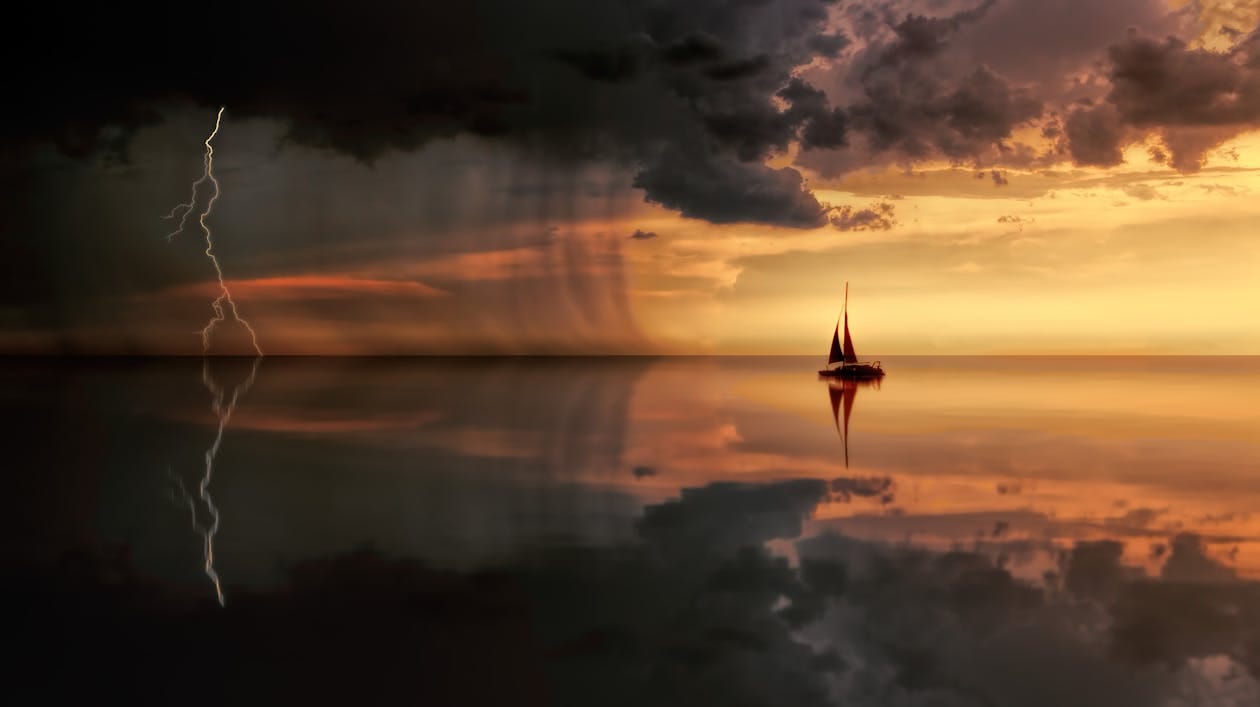 Free A striking seascape featuring a sailboat, lightning, and storm clouds at sunset. Stock Photo