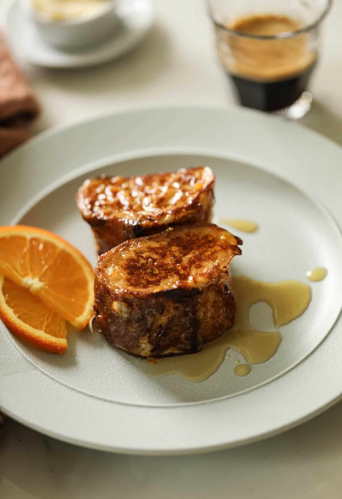 Slices of Pain Perdu, the original French toast, drizzled with syrup on a blue plate with orange slices. 