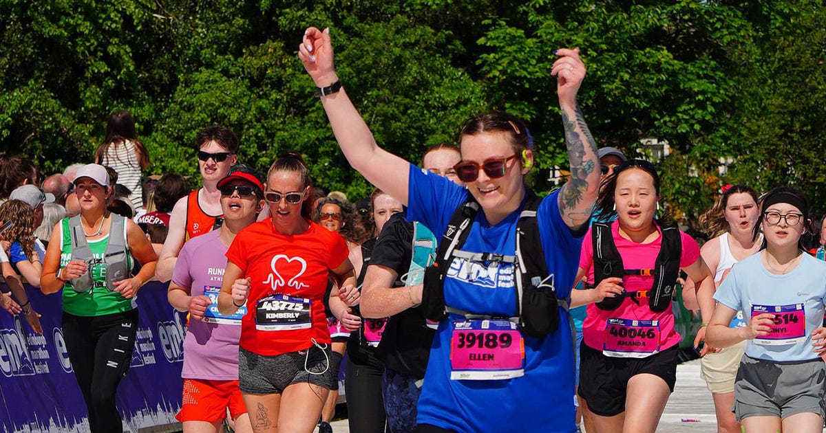 Ellen is at the finish line of a race, wearing sunglasses and a blue tshirt, she's got her arms raised in the air and is celebrating. She's surrounded by other runners. It's a very, very sunny day. Ellen is at the finish line of a race, wearing sunglasses and a blue tshirt, she's got her arms raised in the air and is celebrating. She's surrounded by other runners. It's a very, very sunny day.