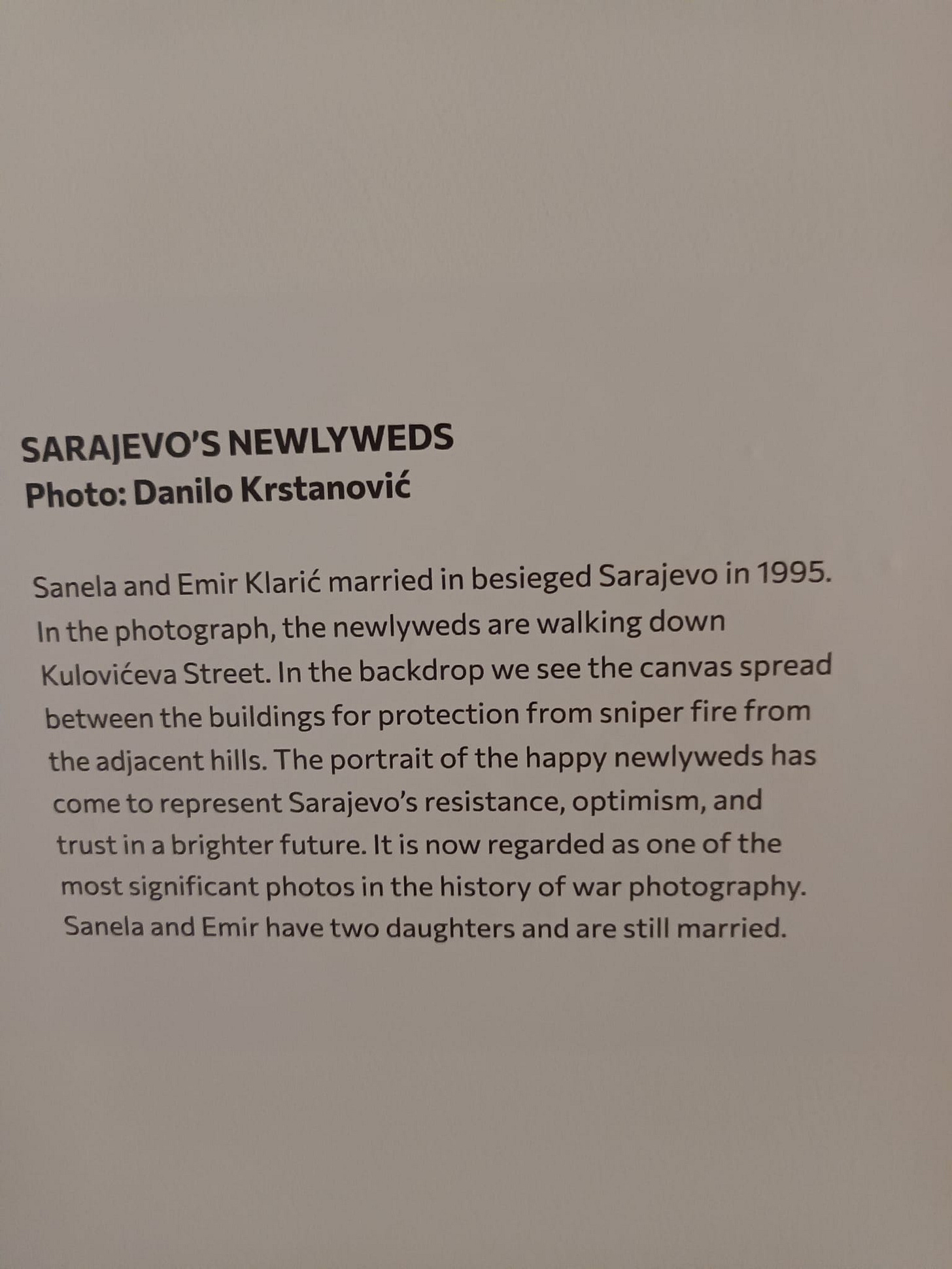 May be an image of text that says "SARAJEVO'S NEWLYWEDS Photo: Danilo Krstanović Sanela and Emir Klarić married in besieged Sarajevo in 1995. In the photograph, the newlyweds are walking down Kulovićeva Street. In the backdrop we see the canvas spread between the buildings for protection from sniper fire from the adjacent hills. The portrait of the happy newlyweds has come to represent Sarajevo's resistance, optimism, and trust in a brighter future. It is now regarded as one of the most significant photos in the history of war photography. Sanela and Emir have two daughters and are still married."