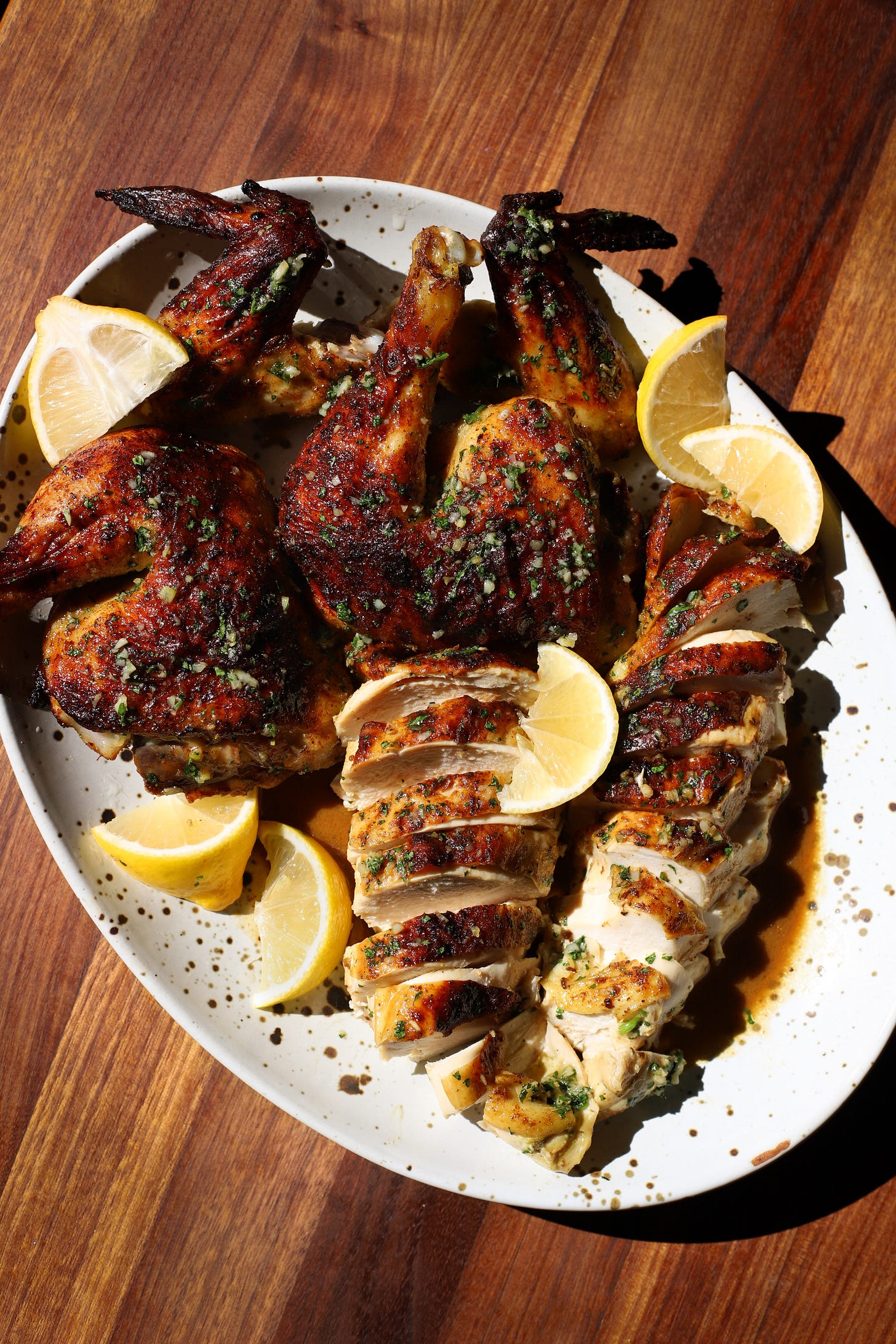 Carved roast chicken with lemon wedges on an oval platter on a wooden table