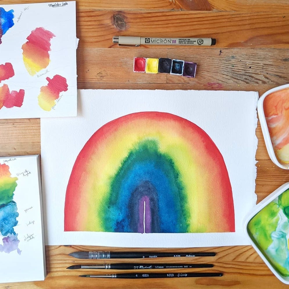 large watercolor rainbow painting on a wooden desk, with pans, brushes and palettes around it large watercolor rainbow painting on a wooden desk, with pans, brushes and palettes around it