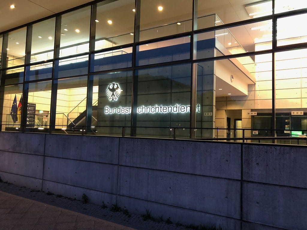 Glass entrance with the federal eagle and Bundesnachrichtendienst lettering above a concrete wall. Glass entrance with the federal eagle and Bundesnachrichtendienst lettering above a concrete wall.