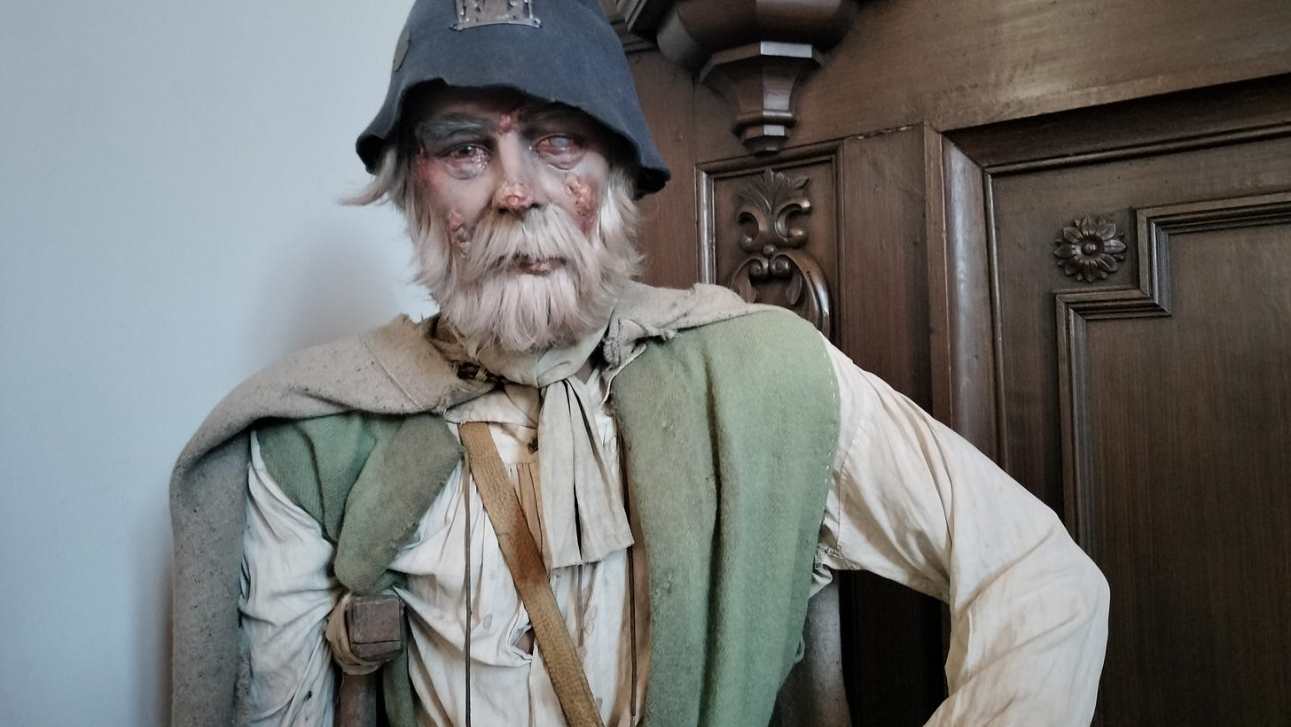A wax statue of a patient dressed in rags and covered in sores