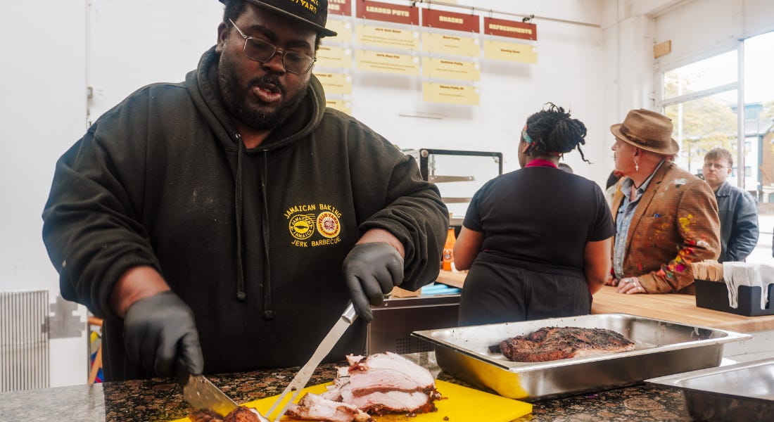 A man - Jowayne Marks - cutting a loin of pork with a queue of people behind him by the counter