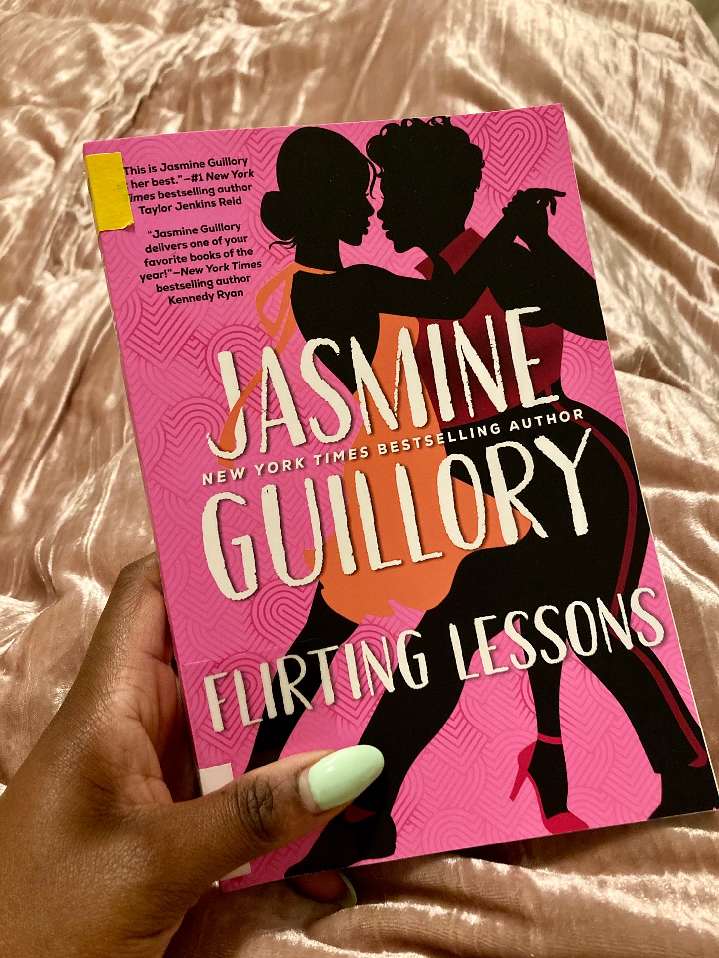 Picture of a Black woman with mint green nails holding a copy of Flirting Lessons by Jasmine Guillory, which is a pink cover featuring the silhouettes of two Black women dancing. Picture of a Black woman with mint green nails holding a copy of Flirting Lessons by Jasmine Guillory, which is a pink cover featuring the silhouettes of two Black women dancing.