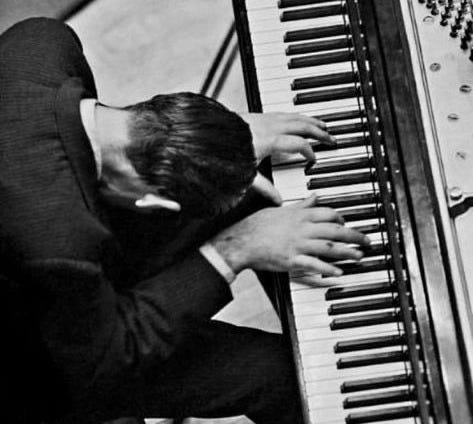 This may contain: a man sitting at a piano with his hands on the keys and head resting against it