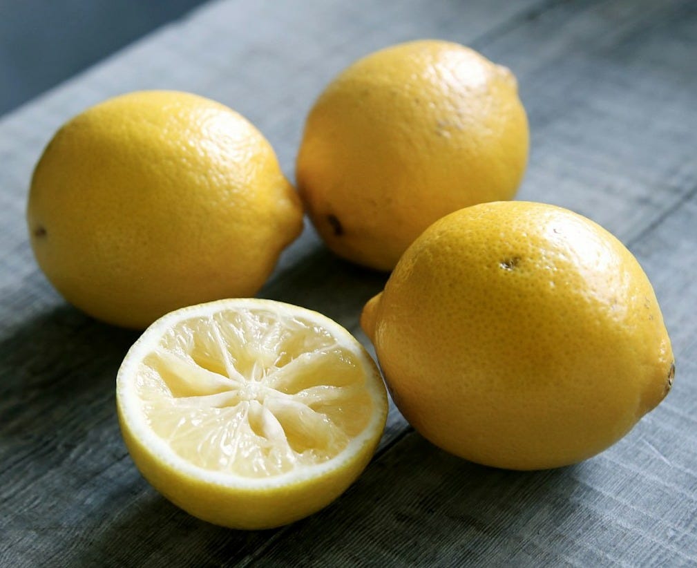 three yellow lemons beside sliced lemon placed on gray wooden surface