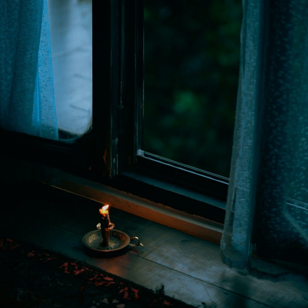 A lit candle sitting in front of a window