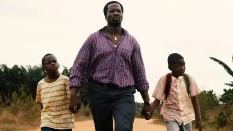 MUBI An actor is walking, holding the hands of two children, in the film