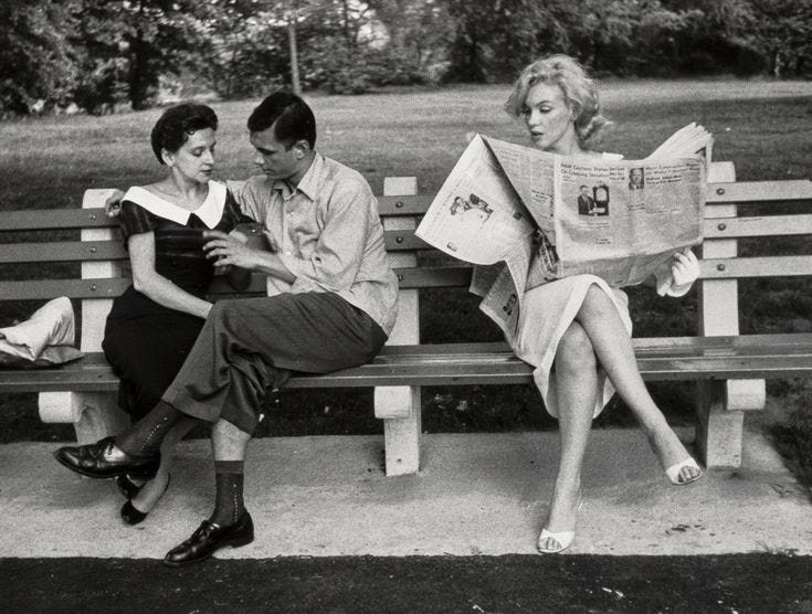 This may contain: three people sitting on a bench reading newspapers